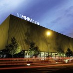 The MHP Arena in Ludwigsburg at dusk, illuminated by streetlights and surrounded by trees. The sky is colored blue and pink., © MHPArena Ludwigsburg