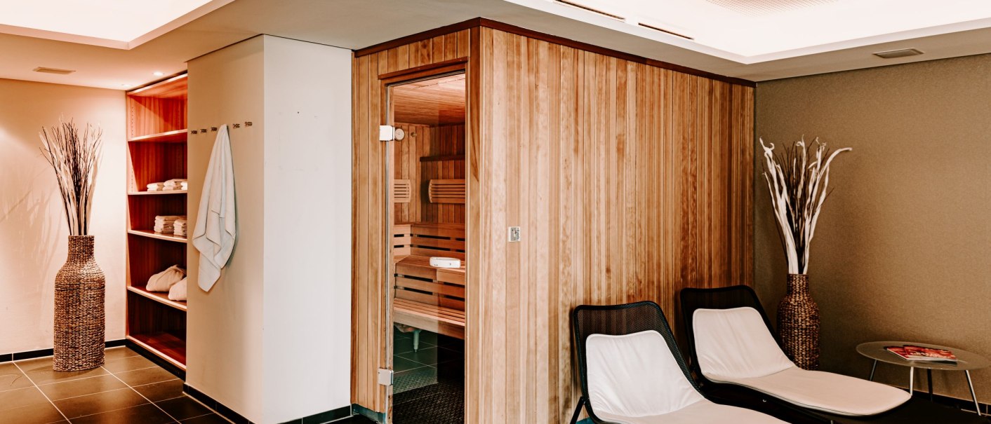 Sauna area with wooden paneling, two loungers, towels and decoration in a modern wellness room., &copy; Vienna House Easy Mo. Stuttgart