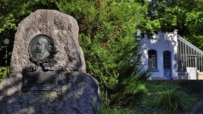 Gedenkstein für Gottlieb Daimler in einem grünen Park, rechts ein weißes Gebäude mit Glasfenstern., © Stuttgart-Marketing GmbH Achim Mende Gedenkstein für Gottlieb Daimler in einem grünen Park, rechts ein weißes Gebäude mit Glasfenstern., © Stuttgart-Marketing GmbH Achim Mende
