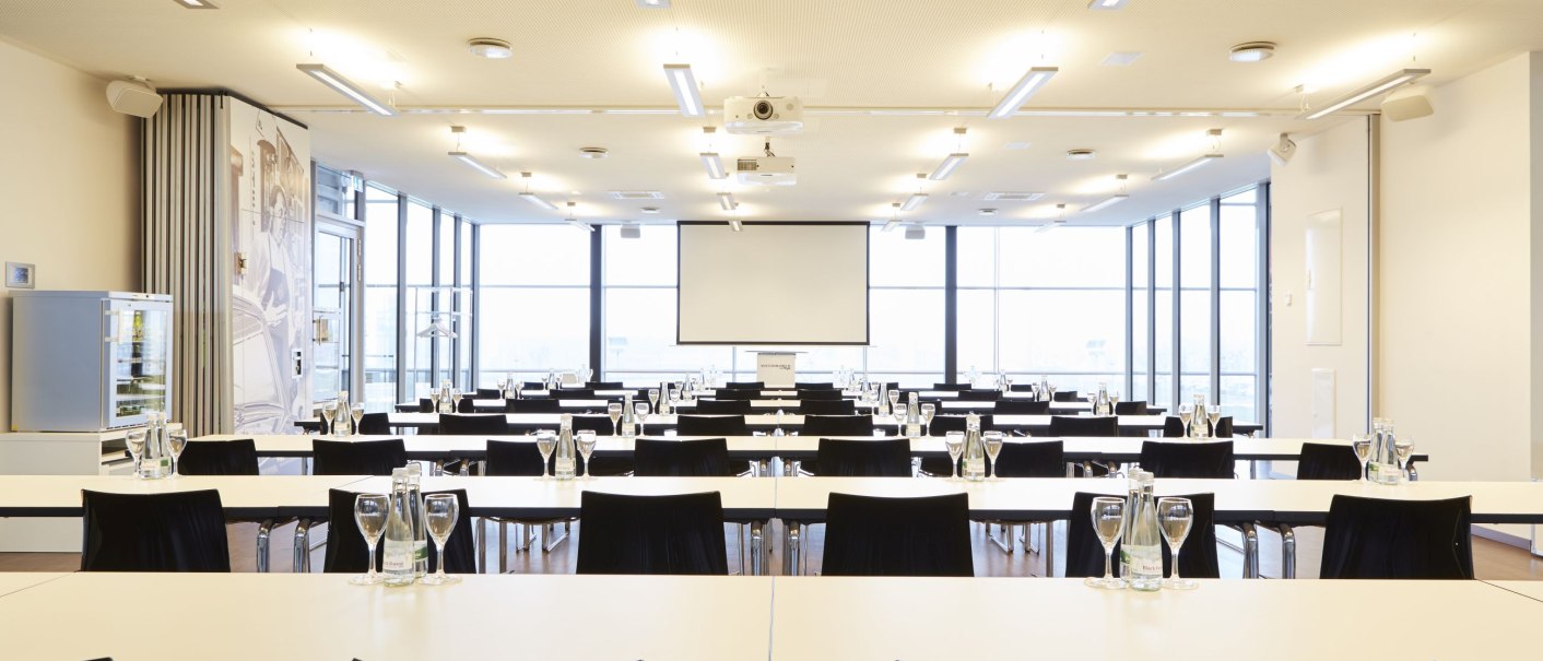 Heller Konferenzraum mit weißen Tischen und schwarzen Stühlen, ausgestattet mit einer Projektionsleinwand und Wassergläsern auf den Tischen., © MW Region Stuttgart