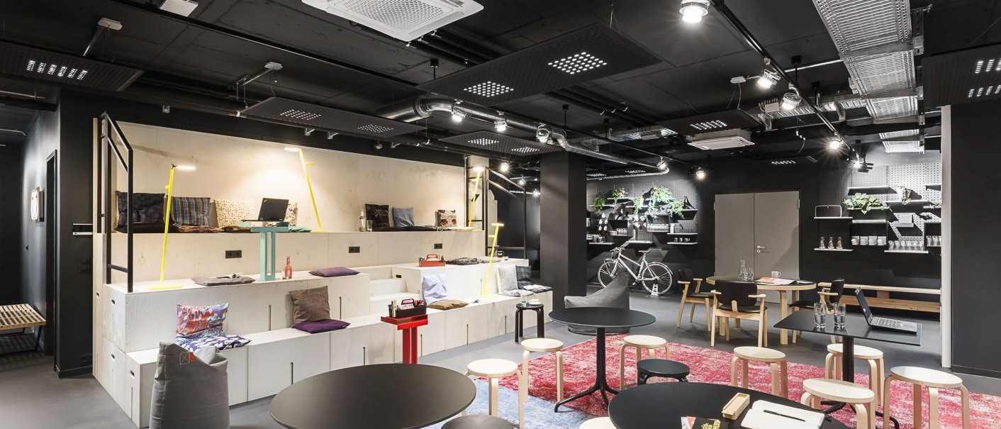 Modernes Coworking-Büro mit Tischen, Stühlen, Regalen, Pflanzen und einem Fahrrad. Helle Beleuchtung und gemütliche Atmosphäre., © Copysign