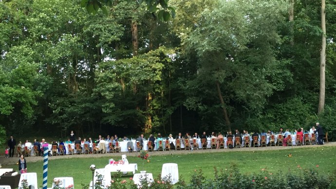 Lange Tafel im Freien, umgeben von Bäumen. Menschen sitzen an festlich gedeckten Tischen im Park von Burg Schaubeck. Sommerliche Atmosphäre., © GFA_GF