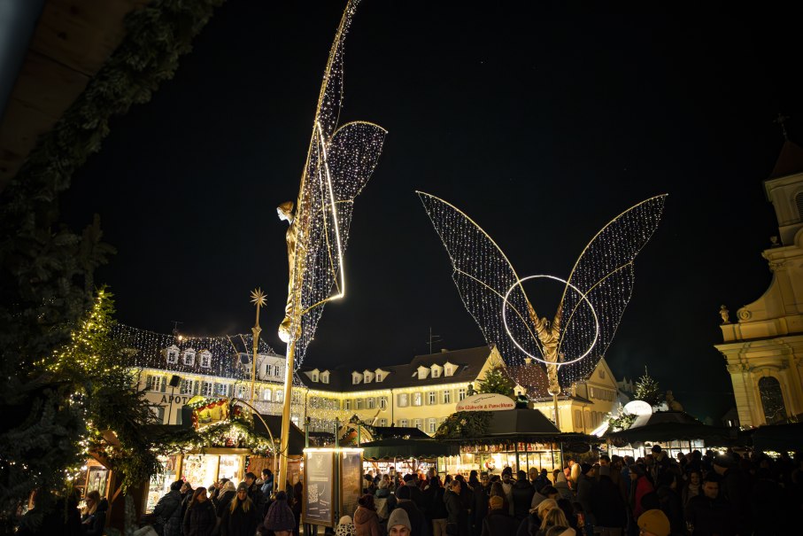 Der Ludwigsburger Barock-Weihnachtsmarkt auf dem Marktplatz bei Nacht, beleuchtete große Engelsfiguren und Buden. Einige Besucherinnen und Besucher tummeln sich auf dem Platz., © Stuttgart Marketing GmbH, Sarah Schmid