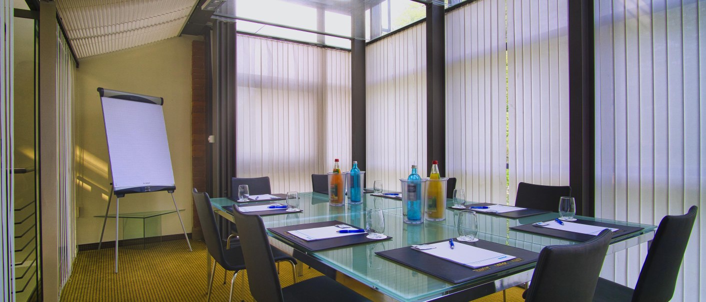 Modern conference room with glass table, chairs and flipchart. There are water bottles and writing materials on the table. Vertical blinds on the windows., &copy; nestor Hotel Ludwigsburg