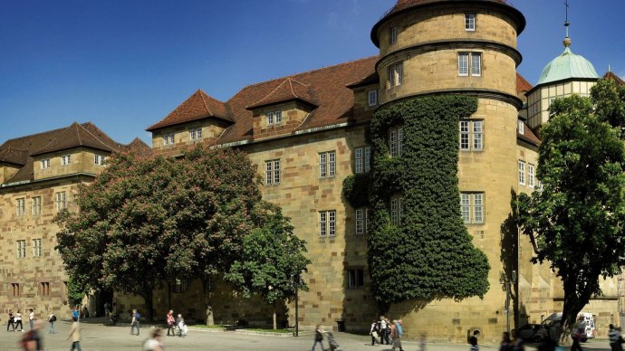 The Old Palace in Stuttgart with overgrown towers and trees in the foreground. People walking on the square in sunny weather., © Stuttgart-Marketing GmbH Florian Selig