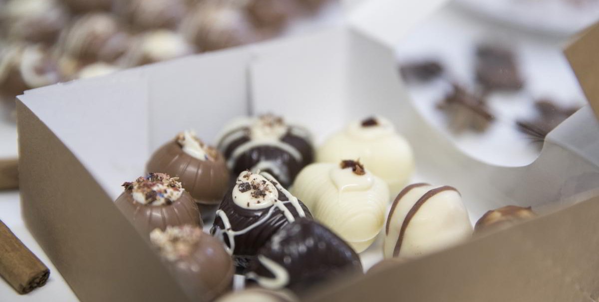Eine Schachtel mit handgemachten Pralinen in verschiedenen Schokoladensorten, dekoriert mit Streuseln und Mustern., © hoponopo GmbH