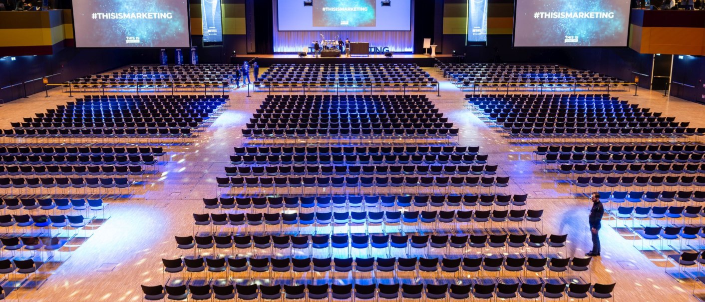 Gro&szlig;er Konferenzsaal in der Messe Stuttgart mit leeren Stuhlreihen, zwei gro&szlig;en Bildschirmen mit der Aufschrift '#THISISMARKETING' und blauer Beleuchtung., &copy; Landesmesse Stuttgart GmbH / Valentin Marquardt