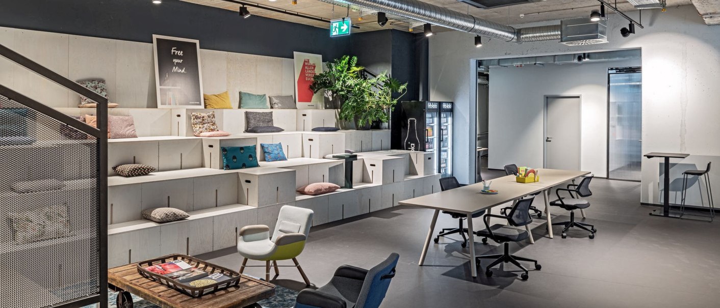 Moderne Lounge mit Sitzstufen, Tischen und Stühlen. Dekoriert mit Kissen, Pflanzen und Wandbildern. Industrieller Stil mit sichtbaren Lüftungsrohren., © Design Offices Moderne Lounge mit Sitzstufen, Tischen und Stühlen. Dekoriert mit Kissen, Pflanzen und Wandbildern. Industrieller Stil mit sichtbaren Lüftungsrohren., © Design Offices