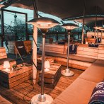 Comfortable seating on a covered upper deck with wooden benches, radiant heaters and blankets. A river can be seen in the background., © Fridas Pier