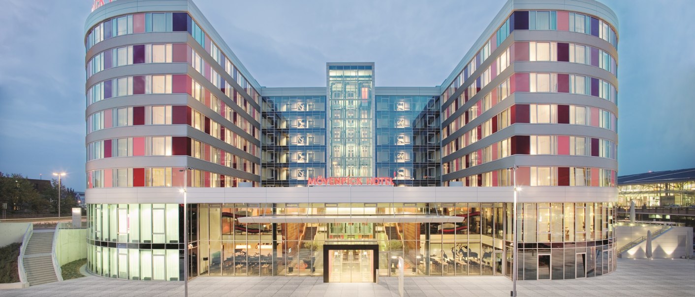 Moderne Fassade des M&ouml;venpick Hotels Stuttgart Airport bei D&auml;mmerung, mit beleuchteten Fenstern und einem gro&szlig;en Eingangsbereich., &copy; M&ouml;venpick Hotel Stuttgart Airport