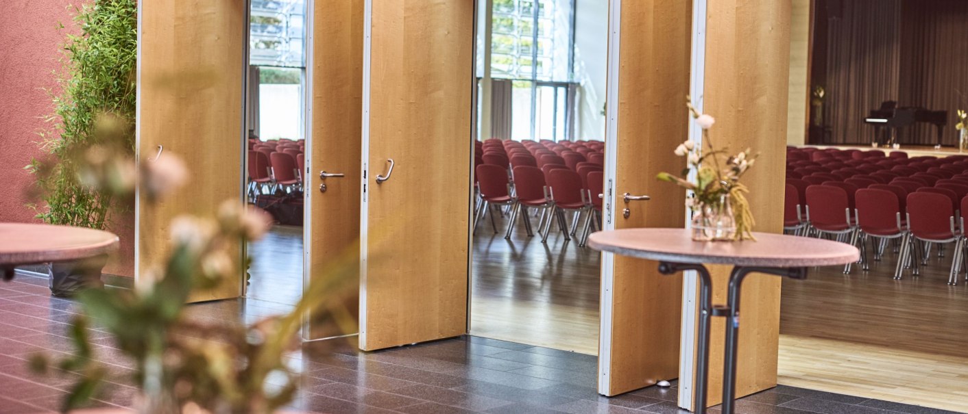 Foyer der Festhalle Schmiden mit offenen Holzt&uuml;ren zum Saal. Rote St&uuml;hle im Hintergrund, Blumen auf Tischen im Vordergrund., &copy; bebopmedia lukas breusch