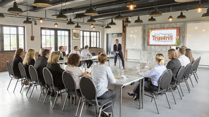 A modern conference room with people sitting at tables. A screen shows the logo of Erlebnispark Tripsdrill., &copy; Claudia Fy