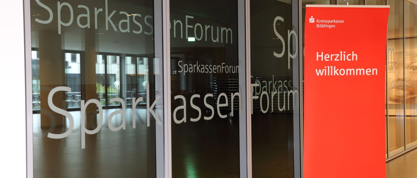 Eingang des SparkassenForums Böblingen mit Glasfront und rotem Banner mit der Aufschrift 'Herzlich willkommen'., © ccbs
