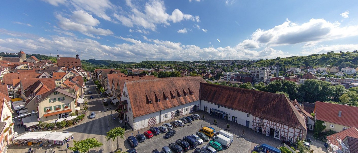 Aerial view of the Alte Kelter town hall in Besigheim, surrounded by traditional buildings and a parking lot with cars. Green hills in the background., © Stadthalle Alte Kelter Besigheim_Achim Mende Aerial view of the Alte Kelter town hall in Besigheim, surrounded by traditional buildings and a parking lot with cars. Green hills in the background., © Stadthalle Alte Kelter Besigheim_Achim Mende