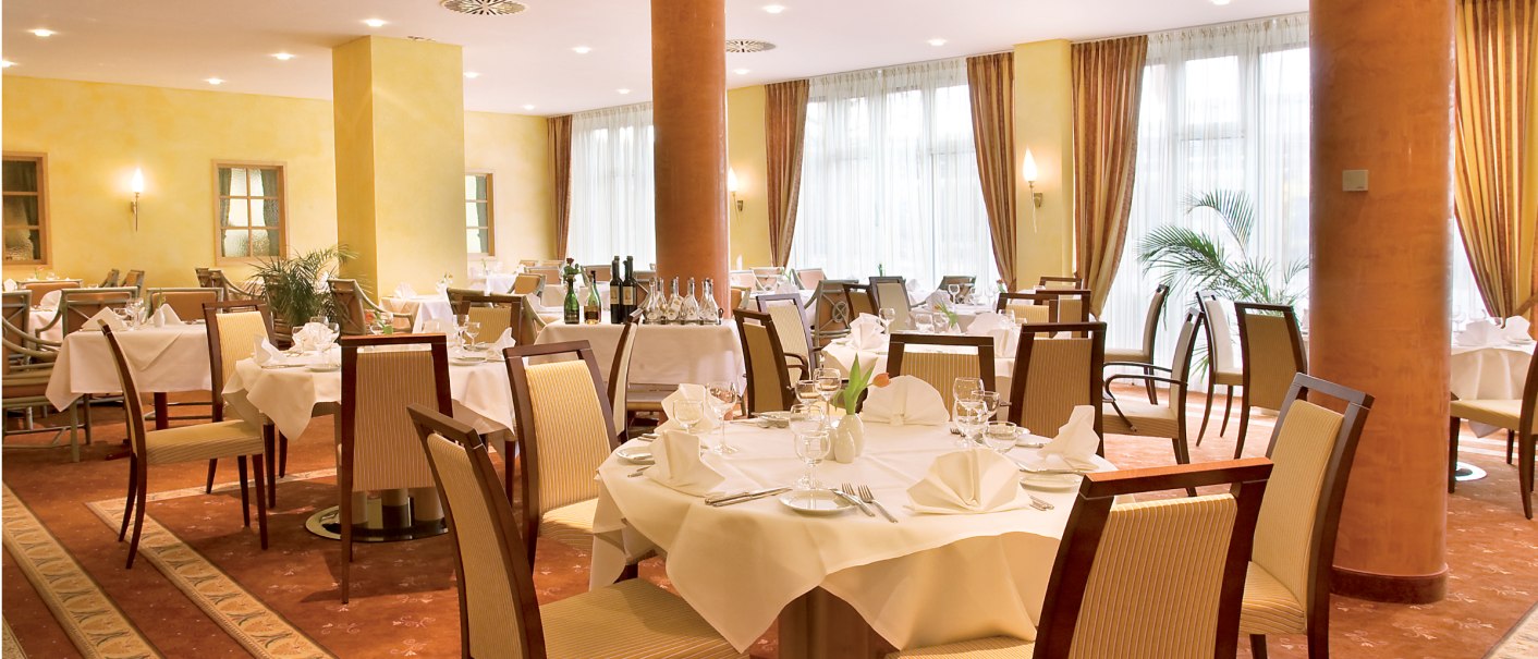Elegantes Restaurant mit gedeckten Tischen, weißen Tischdecken und stilvollen Stühlen. Warme Beleuchtung und große Fenster mit Vorhängen., © eriksonhotel_gf
