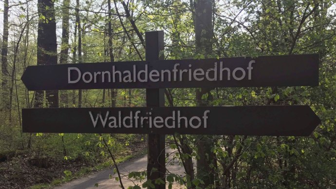 Wegweiser im Wald zeigt zu Dornhaldenfriedhof und Waldfriedhof. Umgeben von Bäumen und grünem Laub., © Stuttgart-Marketing GmbH Wegweiser im Wald zeigt zu Dornhaldenfriedhof und Waldfriedhof. Umgeben von Bäumen und grünem Laub., © Stuttgart-Marketing GmbH