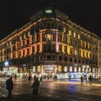 An illuminated building at night with a movie theater and stores on the first floor. People walk past on the street., &copy; Schauspielb&uuml;hnen Stuttgart