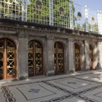 A terrace with a marble floor, ornate wooden doors, and a decorative fence. The sun casts shadows on the floor., &copy; csusannmeissner