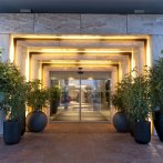 Moderner Hoteleingang mit beleuchteten Rahmen und Glasdrehtür, flankiert von großen Pflanzen in schwarzen Töpfen., © Wyndham Stuttgart Airport Messe