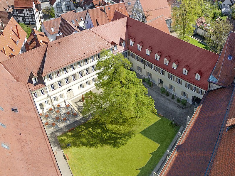 Aerial view of the inner courtyard of Urach Abbey with red roofs, a large tree and surrounding buildings., © Claus Arnold