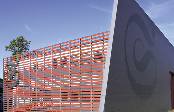 Modern town hall with red slatted fa&ccedil;ade and large logo on a gray wall, surrounded by flowerbeds under a blue sky., &copy; Stadt Marbach a.N.