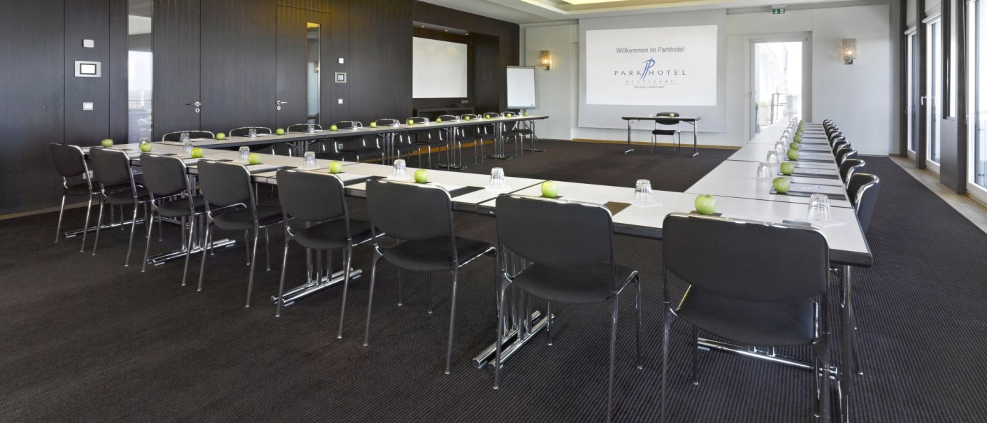 Ein moderner Konferenzraum mit U-förmiger Tischanordnung, Stühlen und grünen Äpfeln auf den Tischen. Ein Projektor zeigt 'Willkommen im Parkhotel'., © Parkhotel Stuttgart Messe-Airport GmbH & Co KG Ein moderner Konferenzraum mit U-förmiger Tischanordnung, Stühlen und grünen Äpfeln auf den Tischen. Ein Projektor zeigt 'Willkommen im Parkhotel'., © Parkhotel Stuttgart Messe-Airport GmbH & Co KG
