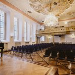 Eleganter Festsaal mit St&uuml;hlen, einem Fl&uuml;gel und einem pr&auml;chtigen Kronleuchter. Die Decke ist kunstvoll bemalt, und gro&szlig;e Fenster lassen viel Licht herein., &copy; NICO KURTH