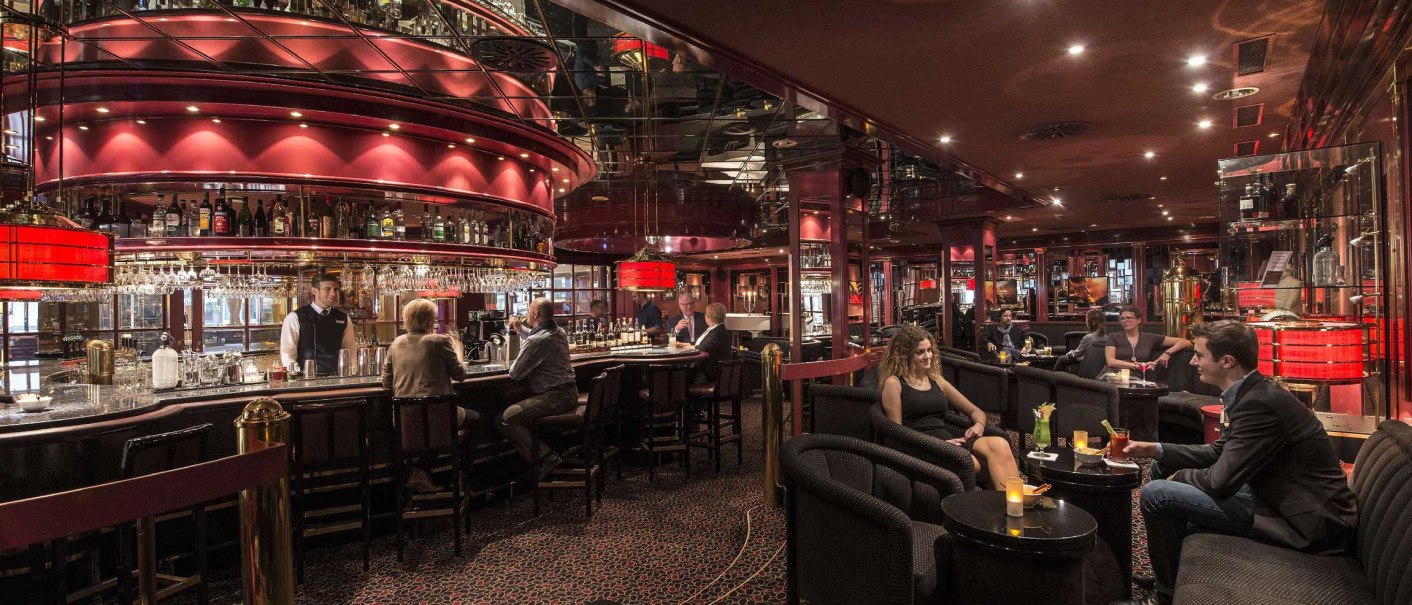 Elegant piano bar in the Maritim Hotel Stuttgart with red decor, guests at the bar and at tables. Cozy atmosphere with subdued lighting., &copy; Maritim Hotelgesellschaft mbH