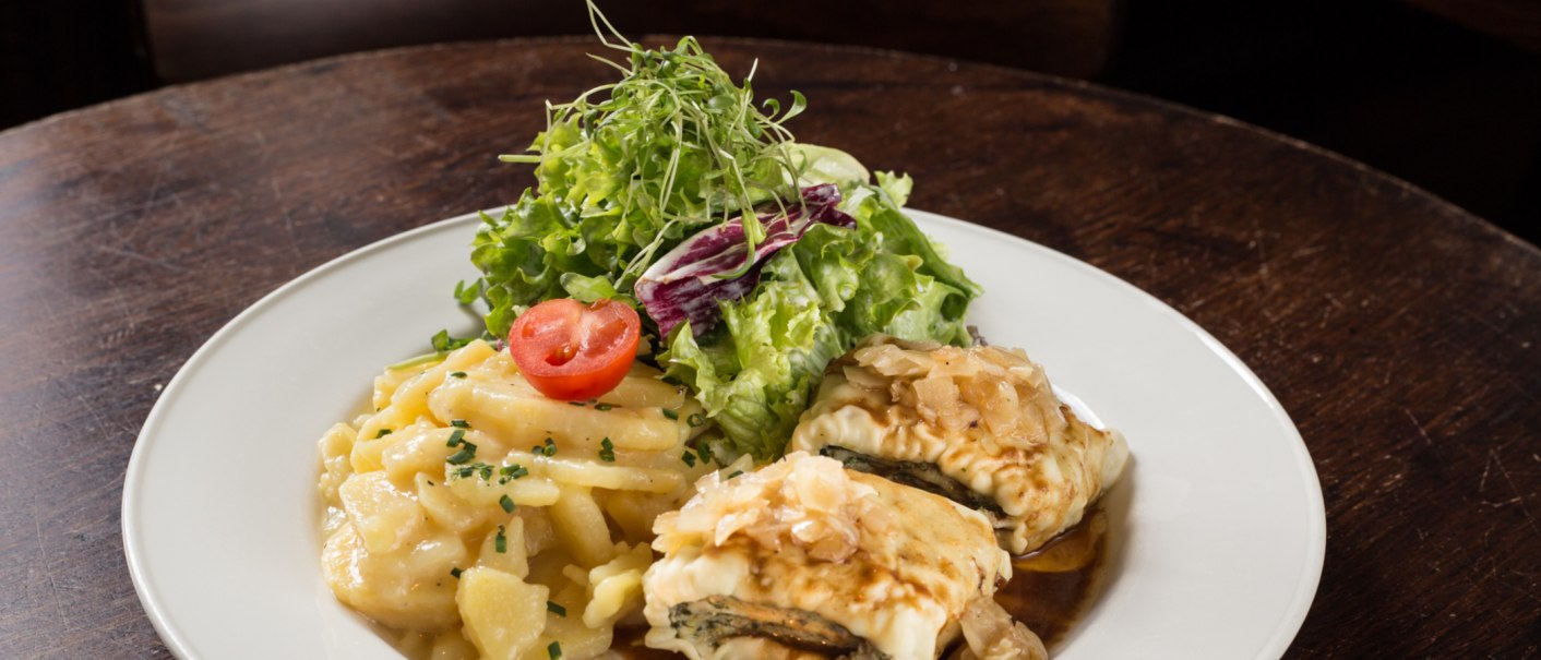 A plate of Maultaschen, potato salad and green salad, garnished with a slice of tomato, on a wooden table., © Amadeus, Stuttgart