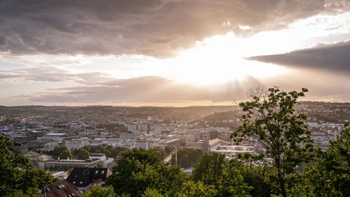 Sonnenuntergang &uuml;ber Stuttgart von der Uhlandsh&ouml;he aus. Die Stadt liegt unter einem bew&ouml;lkten Himmel, durch den Sonnenstrahlen brechen., &copy; Christine Garcia Urbina trickytine