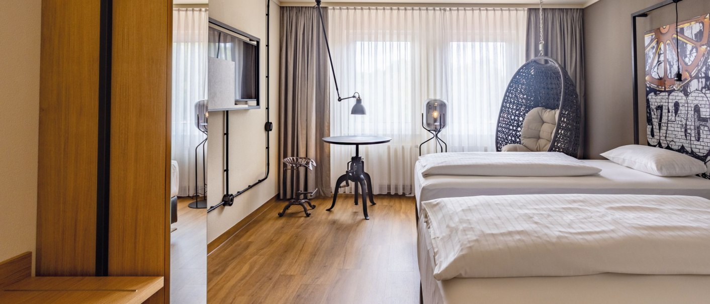 Modernes Hotelzimmer mit zwei Betten, Hängesessel, Tisch und Fernseher. Große Fenster mit Vorhängen lassen viel Licht herein., © Seminaris Hotels (Gerhard Hinz)