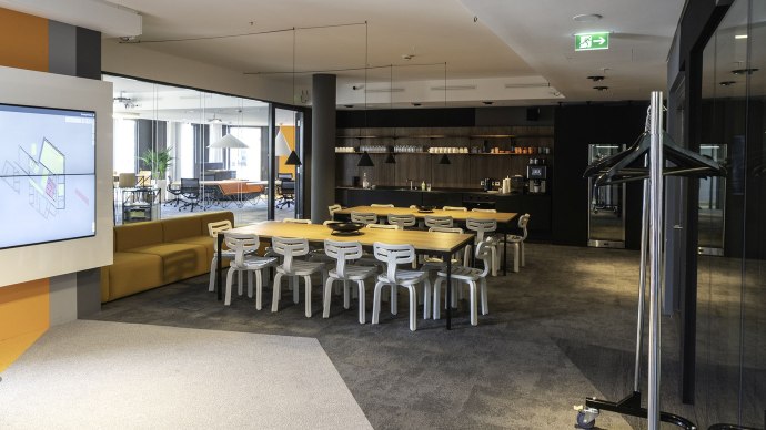 Modern lounge with a large table, white chairs and a kitchenette. Sofas and plants can be seen in the background., &copy; INFOMOTION