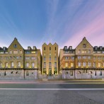Das Arcotel Camino zeigt eine symmetrische Fassade aus Stein mit modernen Elementen, beleuchtet bei Sonnenuntergang. Eine Straße verläuft davor., © ARCOTEL Hotels