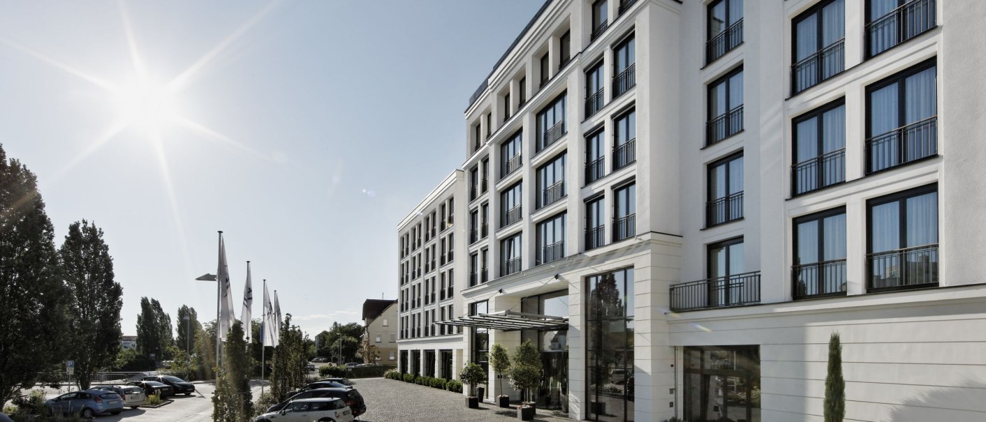 Das Parkhotel Stuttgart Messe-Airport bei Sonnenschein, mit moderner Fassade und gepflastertem Vorplatz. Autos parken entlang der Stra&szlig;e., &copy; Parkhotel Stuttgart Messe-Airport GmbH & Co KG