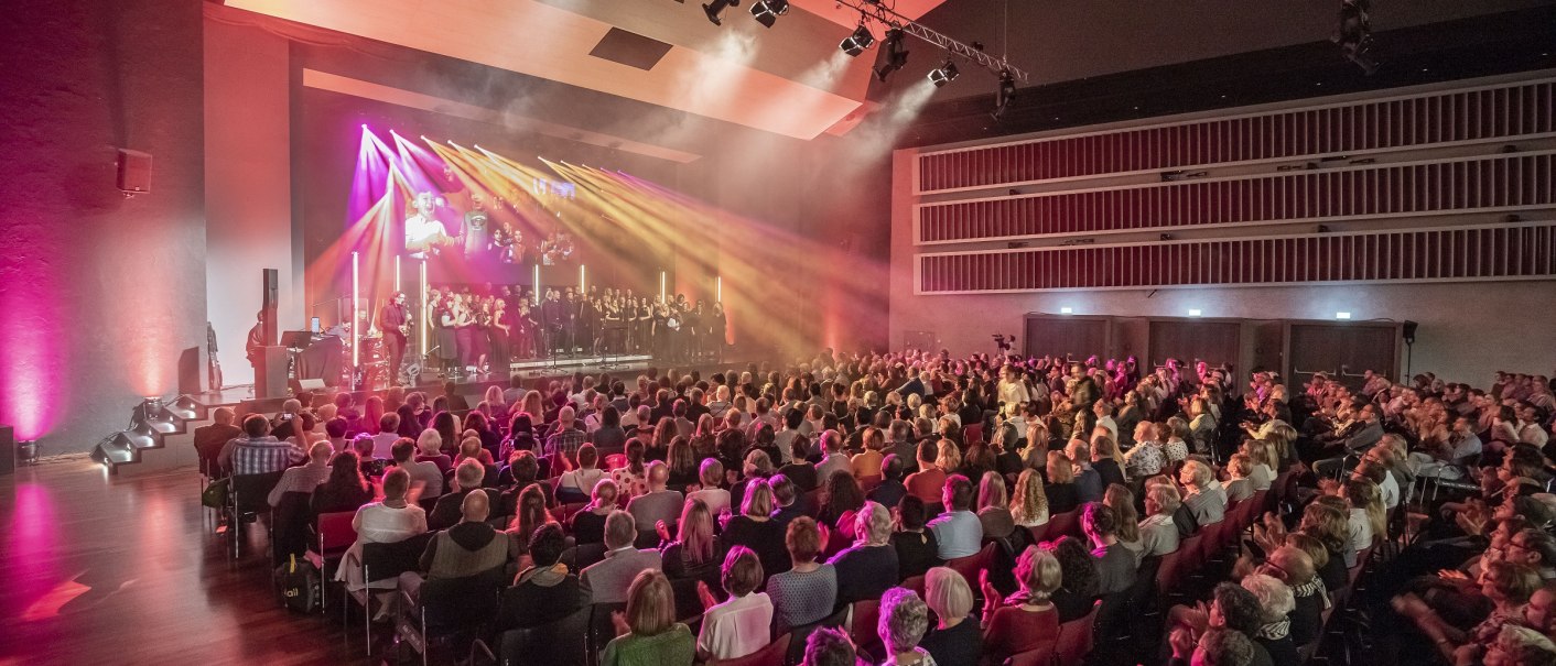 Gro&szlig;er Saal im Neckar Forum mit vollem Publikum und Chor auf der B&uuml;hne, beleuchtet von bunten Lichtern., &copy; eslive