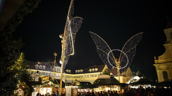 The Ludwigsburg Baroque Christmas Market on the market square at night, with large illuminated angel figures and market stalls. A few visitors are milling about on the square., © Stuttgart Marketing GmbH, Sarah Schmid The Ludwigsburg Baroque Christmas Market on the market square at night, with large illuminated angel figures and market stalls. A few visitors are milling about on the square., © Stuttgart Marketing GmbH, Sarah Schmid