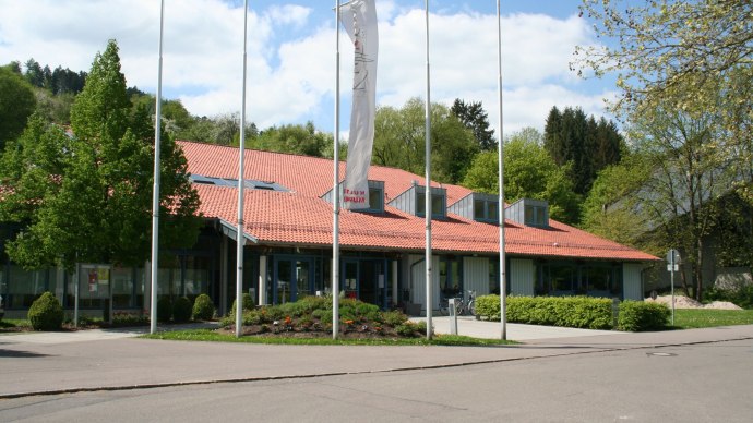The Murrhardt town hall with its red tiled roof, surrounded by trees and flagpoles, on a sunny day., &copy; Stadt Murrhardt
