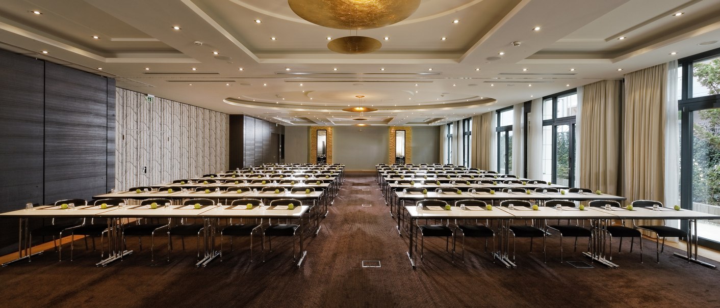 Ein eleganter Ballsaal mit Reihen von Tischen und St&uuml;hlen, modernen Deckenleuchten und gro&szlig;en Fenstern mit Vorh&auml;ngen., &copy; Parkhotel Stuttgart Messe-Airport GmbH & Co KG