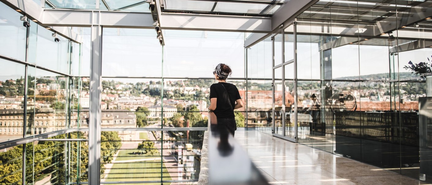 A person stands in the Kunstmuseum Stuttgart and looks through large glass walls at the cityscape., © SMG, Romeo Felsenreich A person stands in the Kunstmuseum Stuttgart and looks through large glass walls at the cityscape., © SMG, Romeo Felsenreich