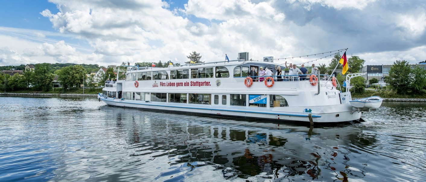 The passenger ship MS Wilhelma is sailing on a river. The sky is blue with clouds. People are standing on board and a German flag is flying at the stern., © all copyrights are reserved by maks richter