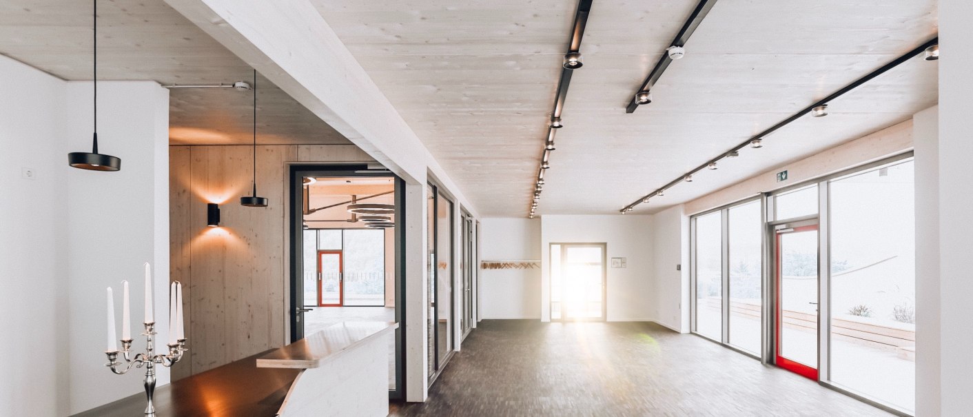 Modernes Foyer mit Holzdecke, Parkettboden, großen Fenstern und einem Tresen mit Kerzenhalter., © Weingaertner-Esslingen-eG