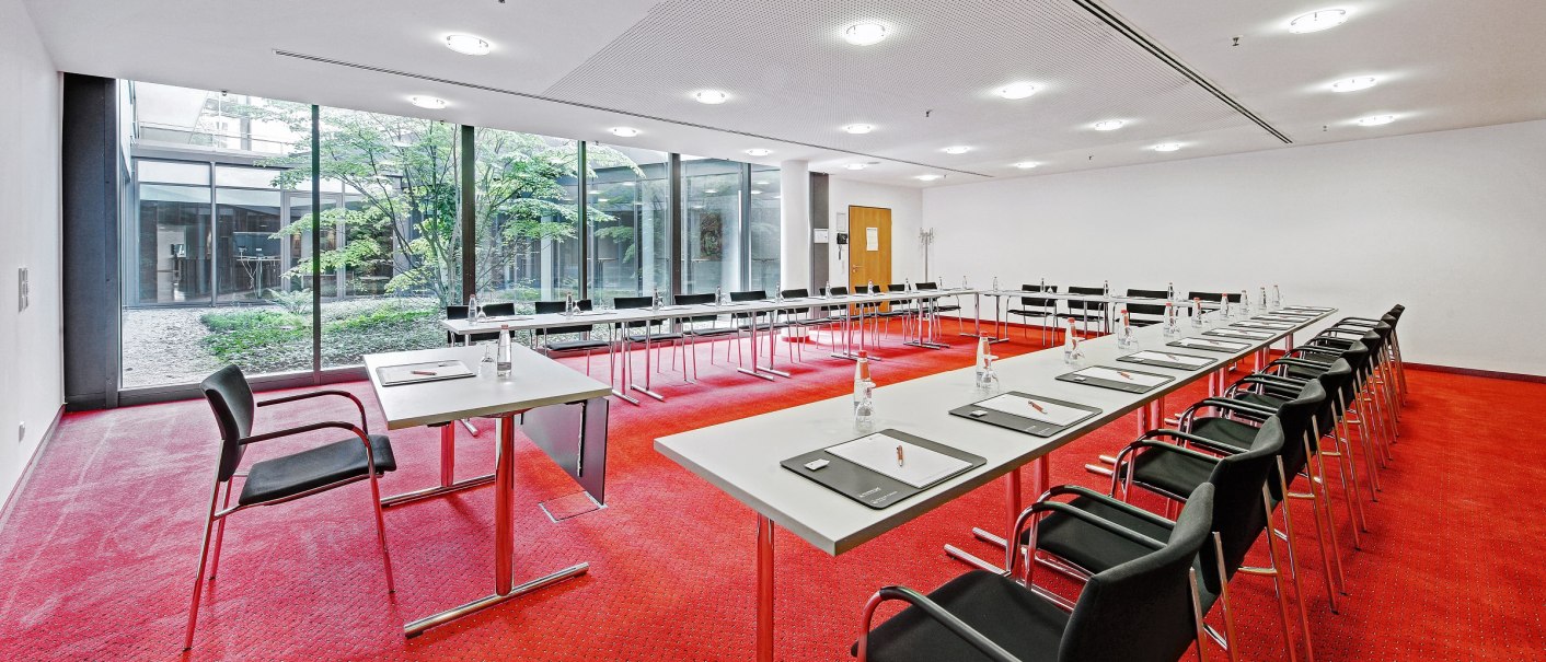 Modern conference room with red carpeting, white tables and black chairs. Large windows offer a view of a green inner courtyard., © Martin Frey Modern conference room with red carpeting, white tables and black chairs. Large windows offer a view of a green inner courtyard., © Martin Frey