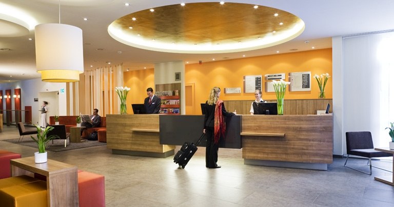 Modern hotel lobby with reception desk where guests check in. The interior is decorated in warm colors, with plants and seating areas., &copy; Mercure Stuttgart Airport Messe