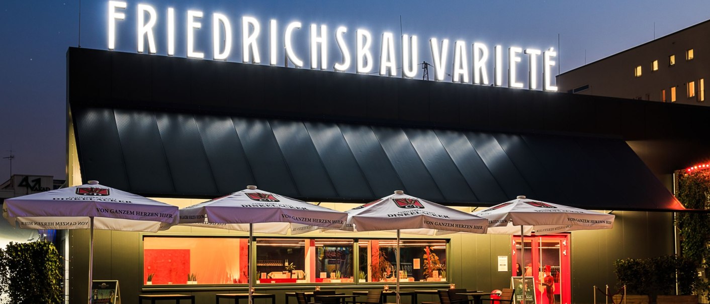 Das Friedrichsbau Varieté bei Nacht, beleuchteter Schriftzug, Sonnenschirme und Tische im Vordergrund., © Friedrichsbau Varieté Das Friedrichsbau Varieté bei Nacht, beleuchteter Schriftzug, Sonnenschirme und Tische im Vordergrund., © Friedrichsbau Varieté