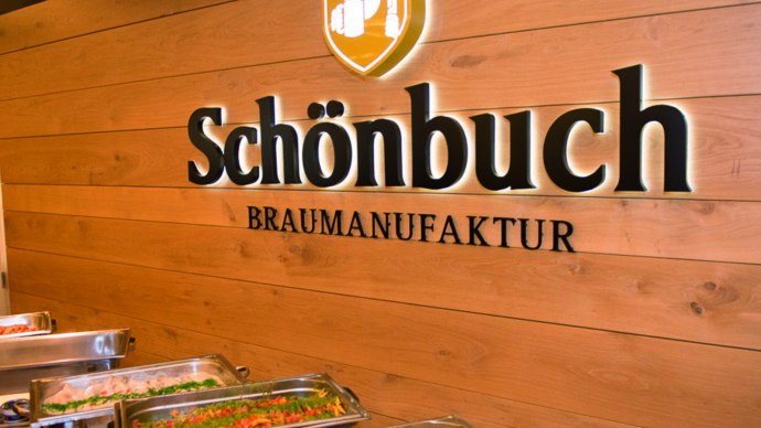Interior view of a brewery with buffet. "Schönbuch Braumanufaktur" is written on the wooden wall. In the foreground are dishes in warming containers., © © Schönbuchbrauerei, Sebastian Berger Interior view of a brewery with buffet. "Schönbuch Braumanufaktur" is written on the wooden wall. In the foreground are dishes in warming containers., © © Schönbuchbrauerei, Sebastian Berger