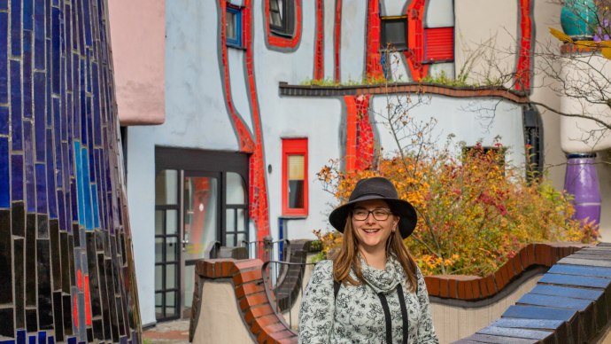 Frau mit Hut vor dem farbenfrohen Hundertwasserhaus in Plochingen, umgeben von herbstlichen Bl&auml;ttern., &copy; Bildergalerie Attila