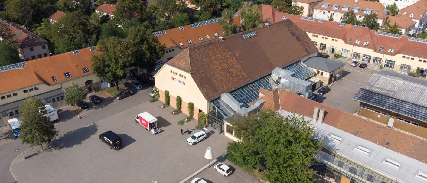 Aerial view of the Phoenixhalle with red roofs, surrounded by trees and parked cars. Residential buildings and green landscape in the background., &copy; Marc Sporys
