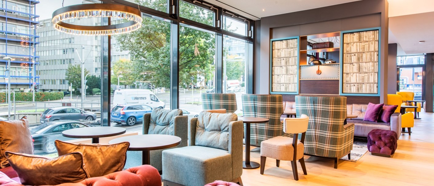 A modern lobby with colorful armchairs, sofas, and tables. Large windows offer a view of the street. Stylish lighting and decor., &copy; Guenter Lenz