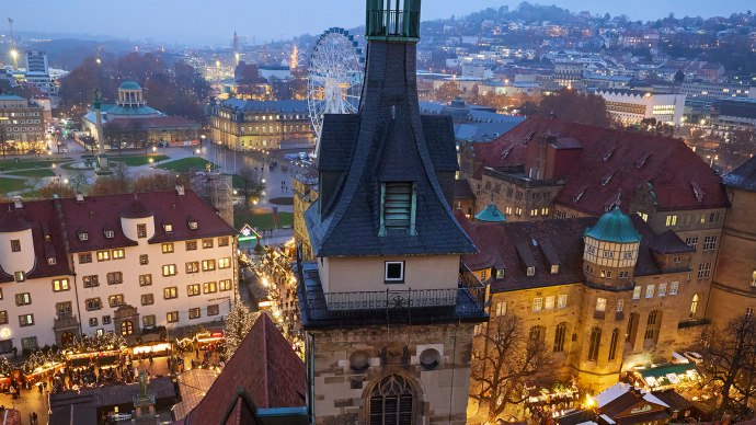 View of Schillerplatz and the Old Palace in Stuttgart at dusk. The Christmas market is illuminated, with a Ferris wheel in the background., © Stuttgart Marketing GmbH View of Schillerplatz and the Old Palace in Stuttgart at dusk. The Christmas market is illuminated, with a Ferris wheel in the background., © Stuttgart Marketing GmbH