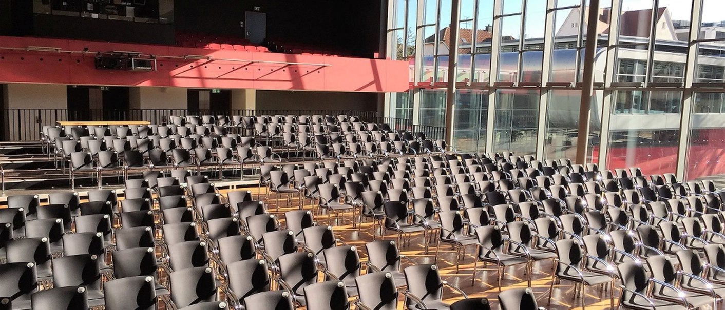 A large hall with lots of empty chairs, large windows and a gallery. Sunlight falls through the windows onto the floor., &copy; k3nmaisch